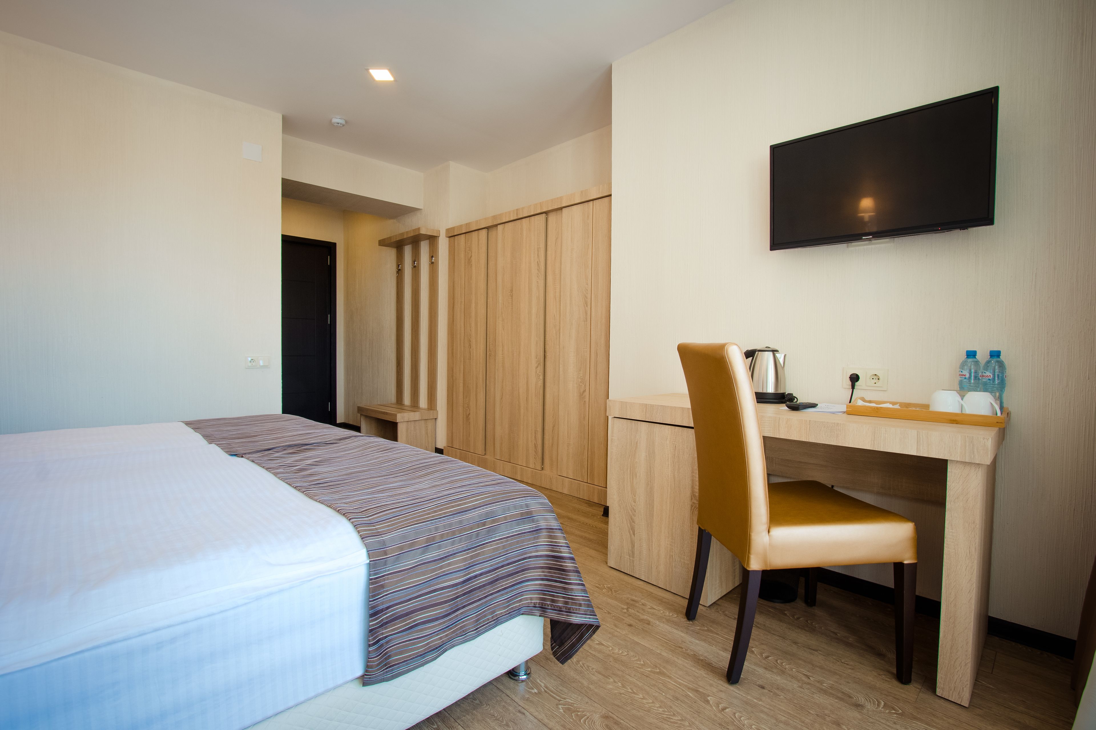 A hotel room with a bed, a desk, a chair, a television, and a wardrobe.
