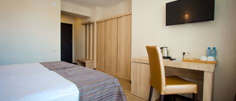 A hotel room with a bed, a desk, a chair, a television, and a wardrobe.