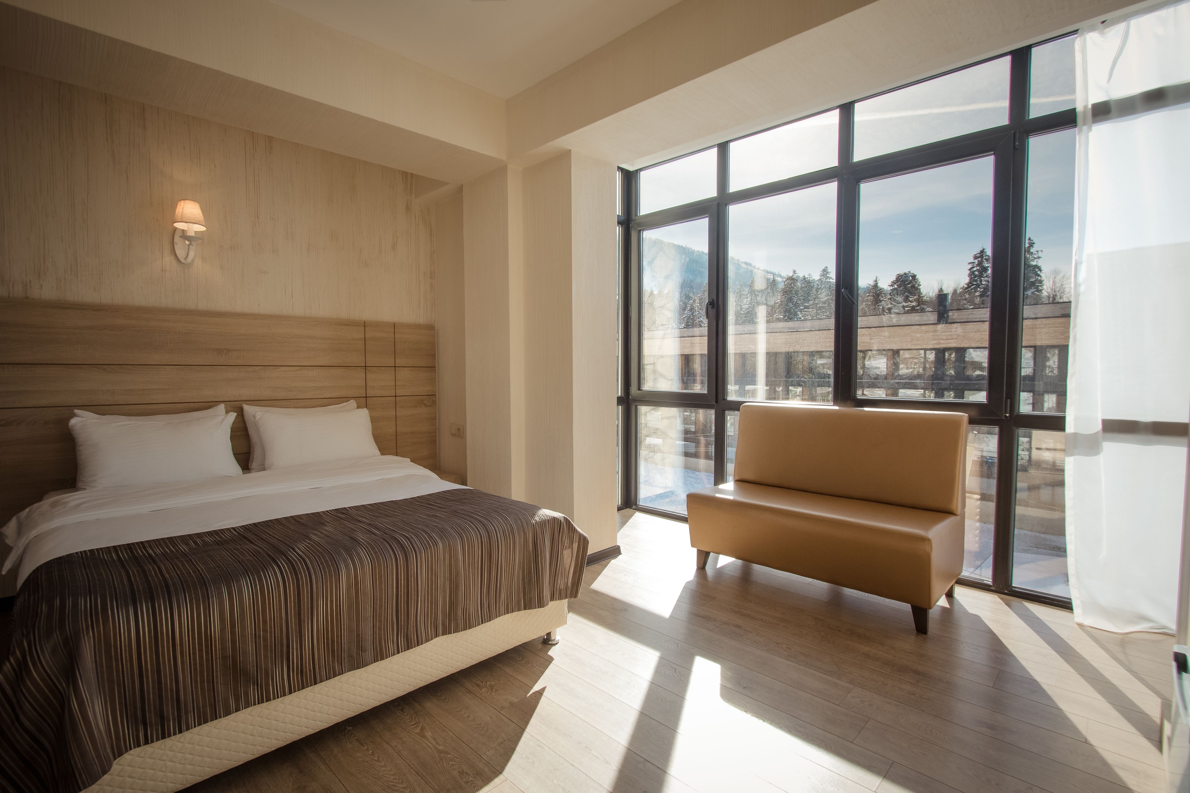 Un dormitorio moderno con una cama grande, un sofá y vistas de un edificio a través de amplios ventanales.