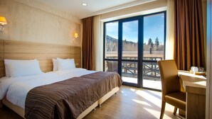 A hotel room with a large bed, a desk, and a view of a mountain landscape. - BM Plaza (Borjomi)