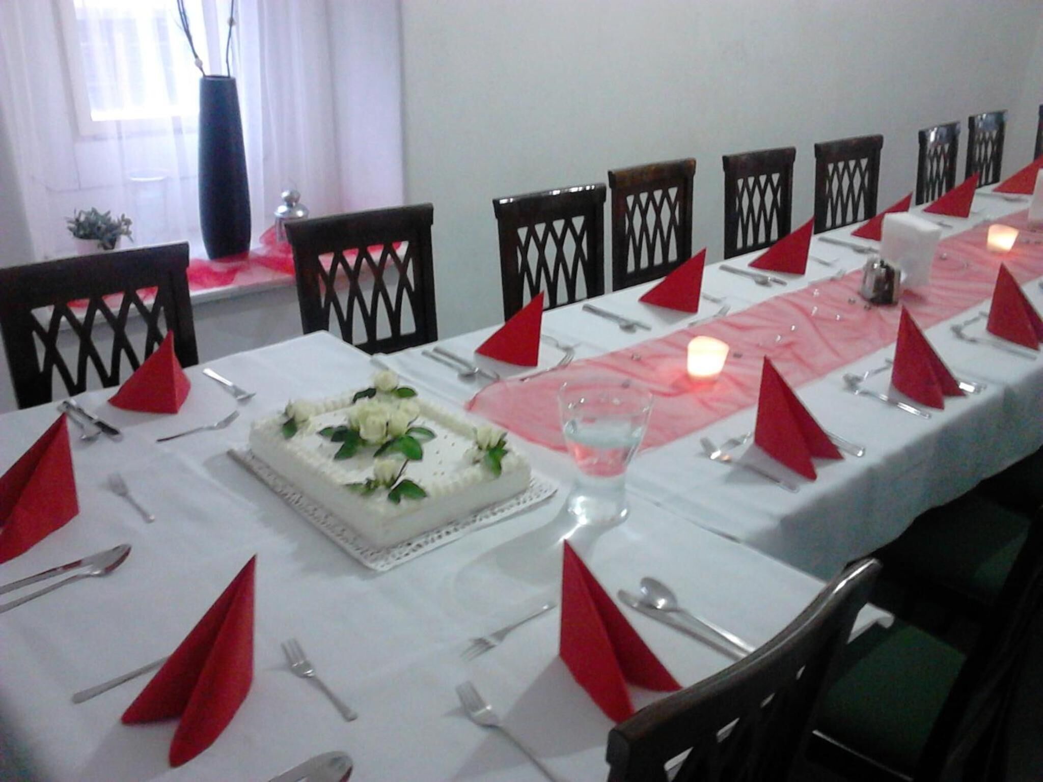 Een eettafel gedekt met rode servetten, bestek en een middelpuntstuk met witte bloemen.