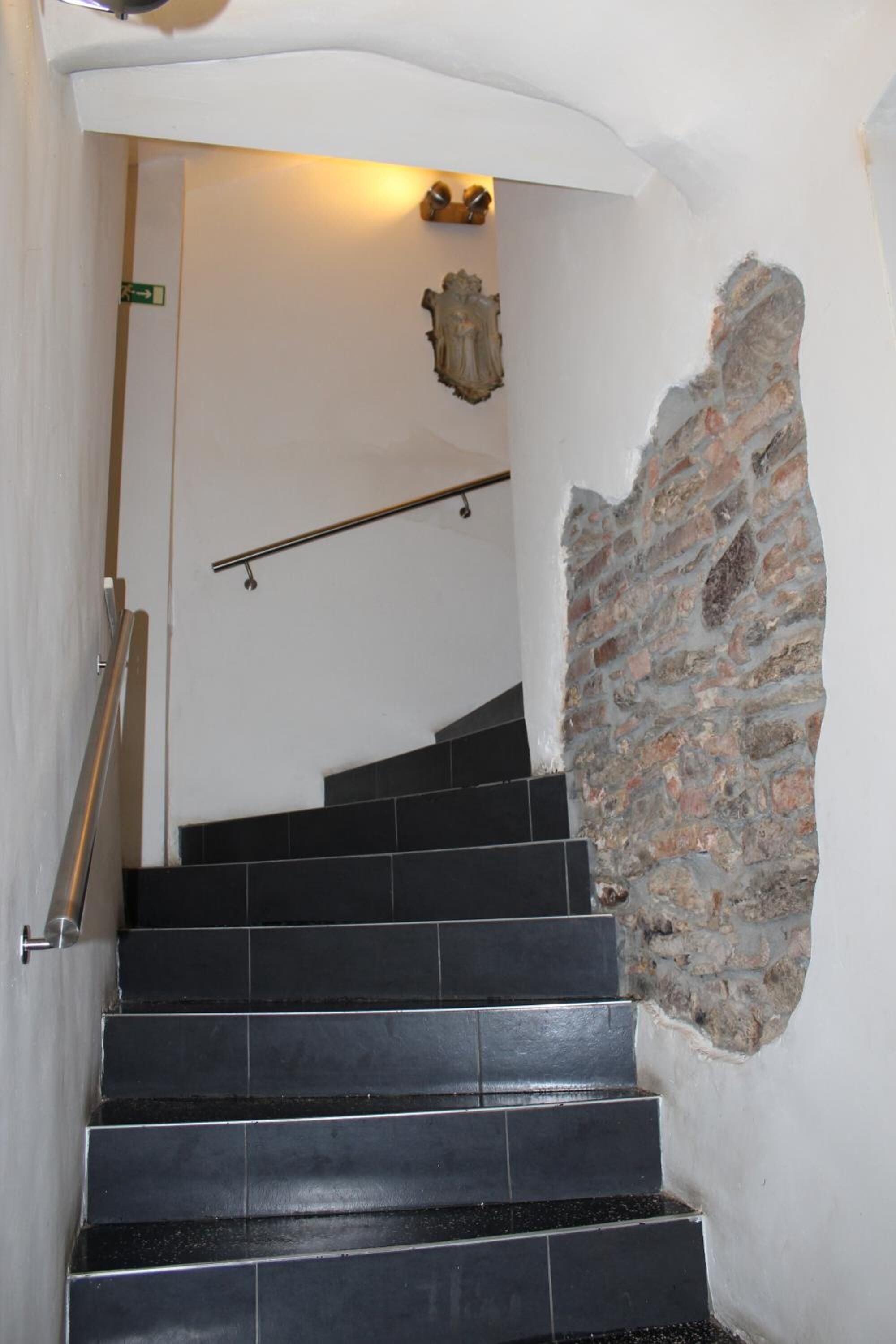 A staircase with black tiles, a stone wall, and a metal handrail.