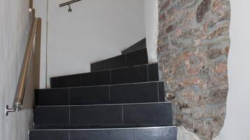 A staircase with black tiles, a stone wall, and a metal handrail.