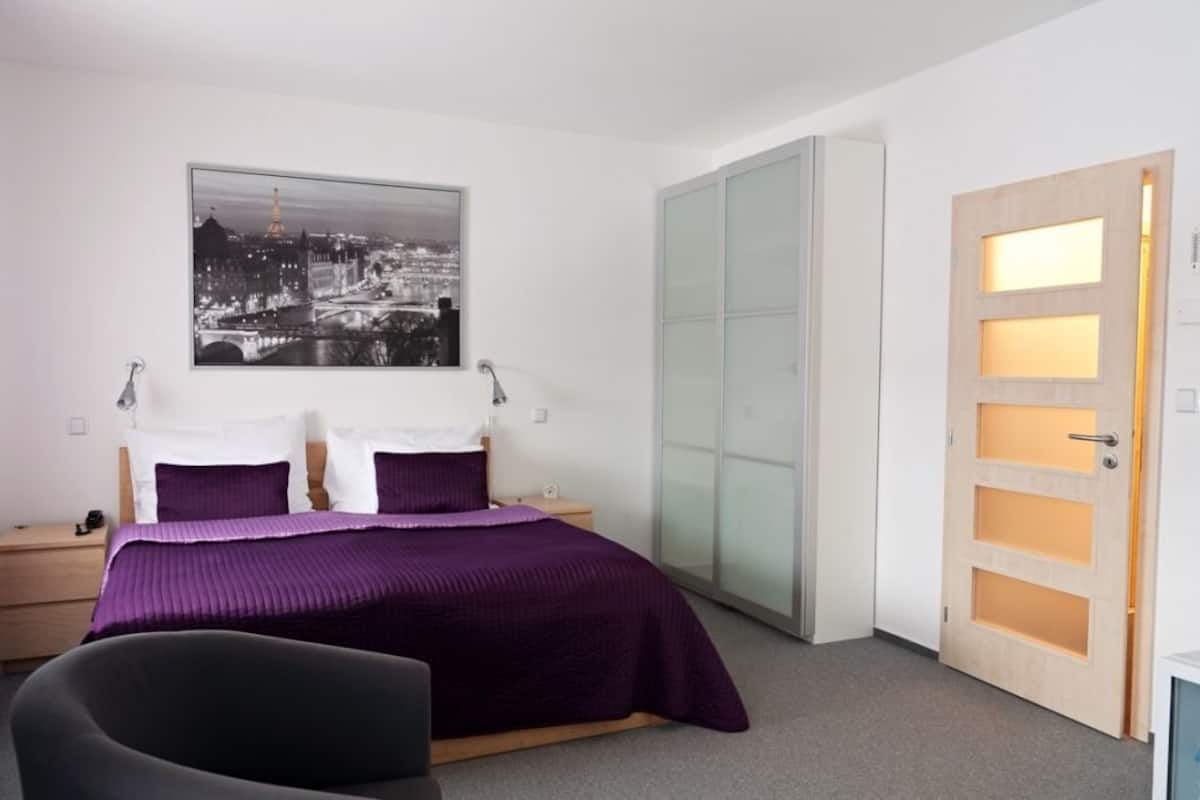 A bedroom with a bed, a nightstand, a chair, a wardrobe, and a door.