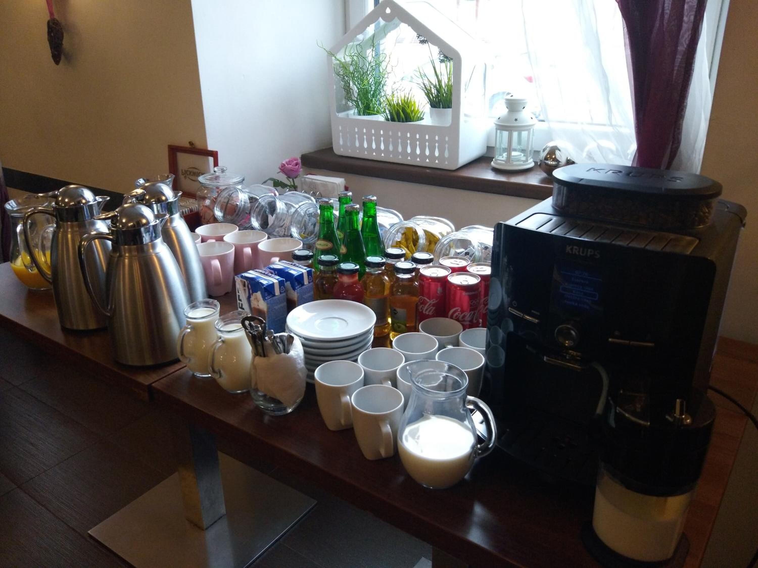 Montaje de un bufé de desayuno con diversos alimentos y bebidas, incluyendo cafeteras, jarras de leche y botellas.