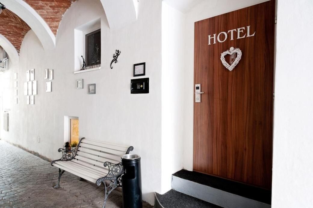 A hotel entrance with a wooden door labeled "HOTEL," a bench, and framed pictures on the wall.