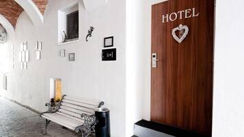 A hotel entrance with a wooden door labeled "HOTEL," a bench, and framed pictures on the wall.
