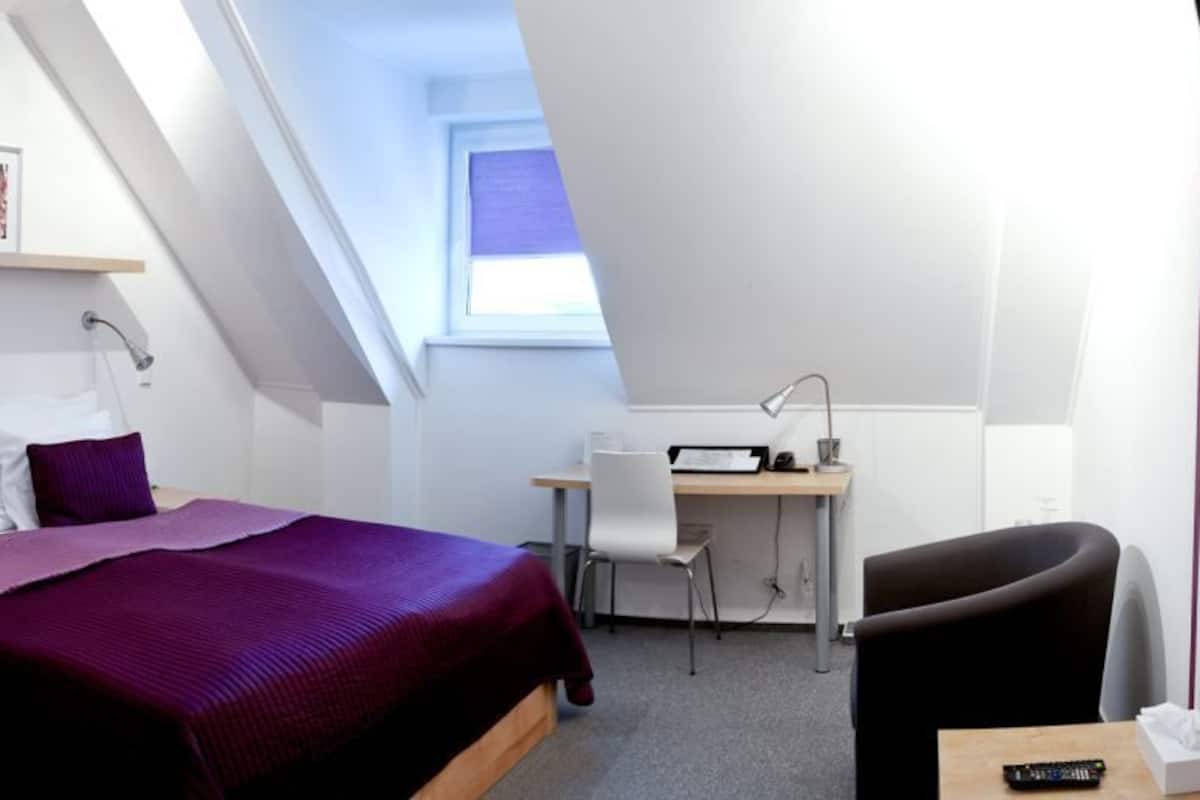 A bedroom with a bed, desk, chair, and a window.