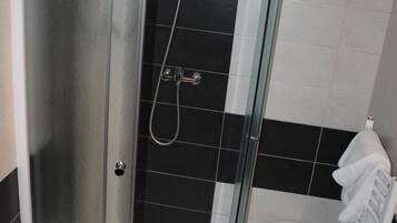 A shower area with a glass door, a white towel rack, and a small stool.
