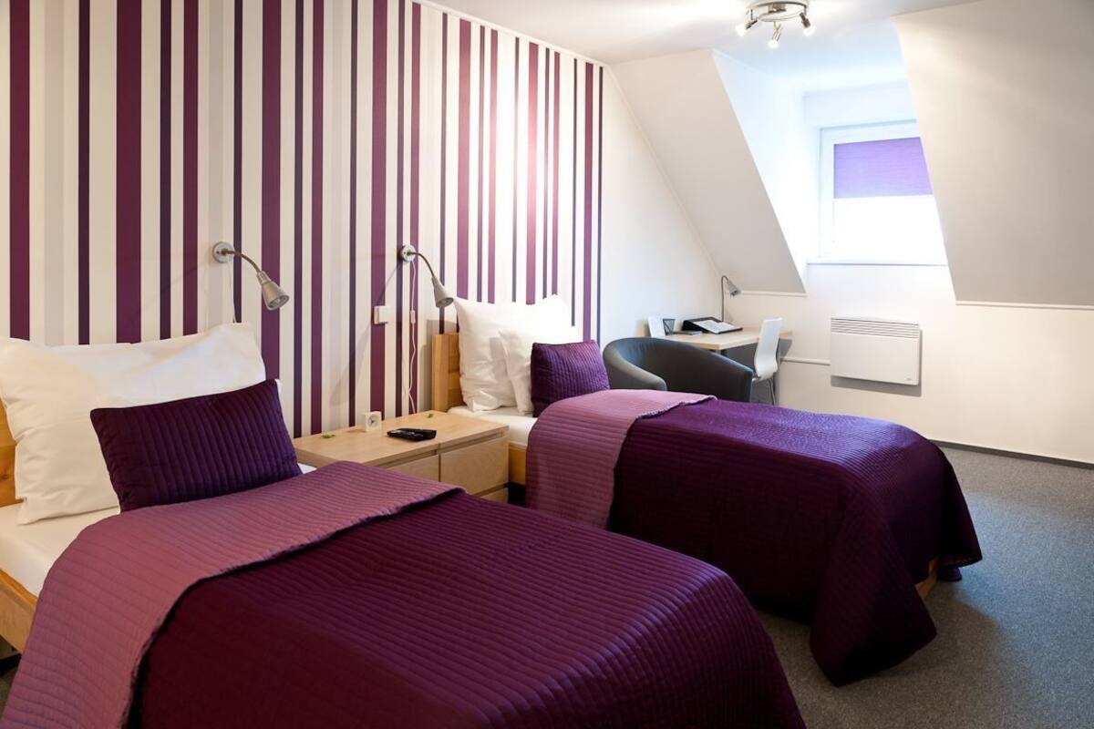 A hotel room with two beds, a desk, a chair, and a window.