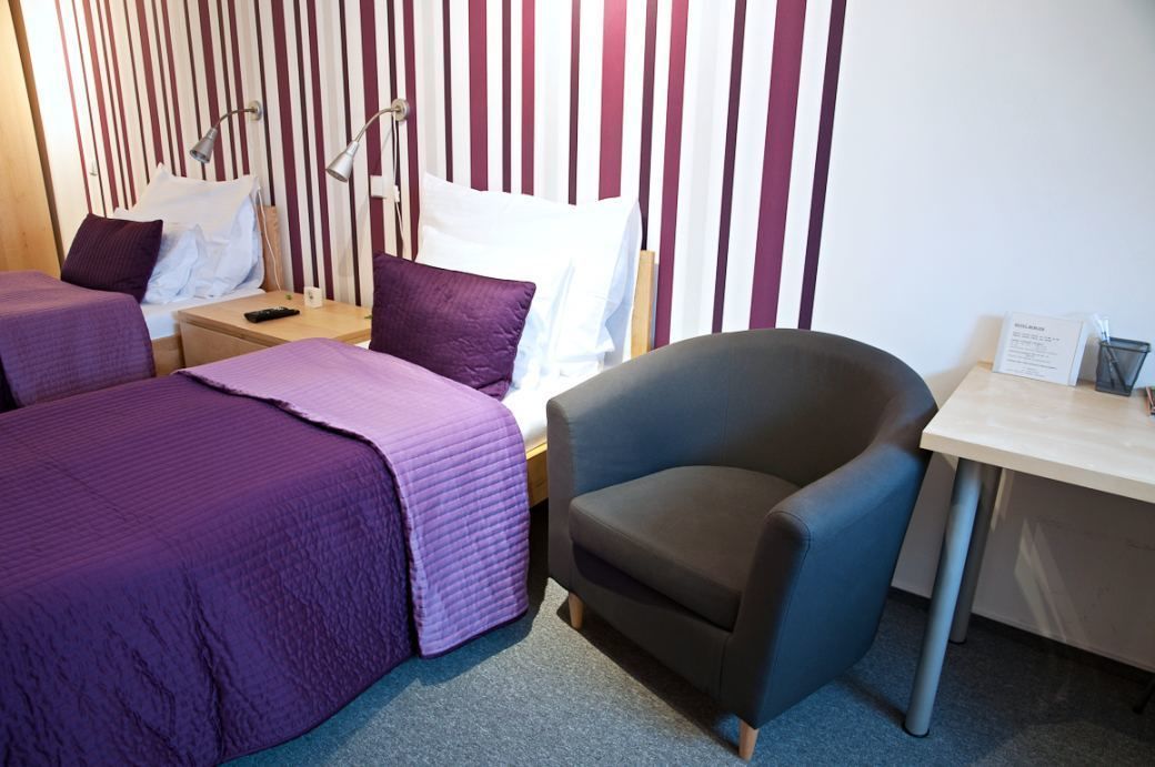 A hotel room with two beds, a desk, a chair, and a striped wall.