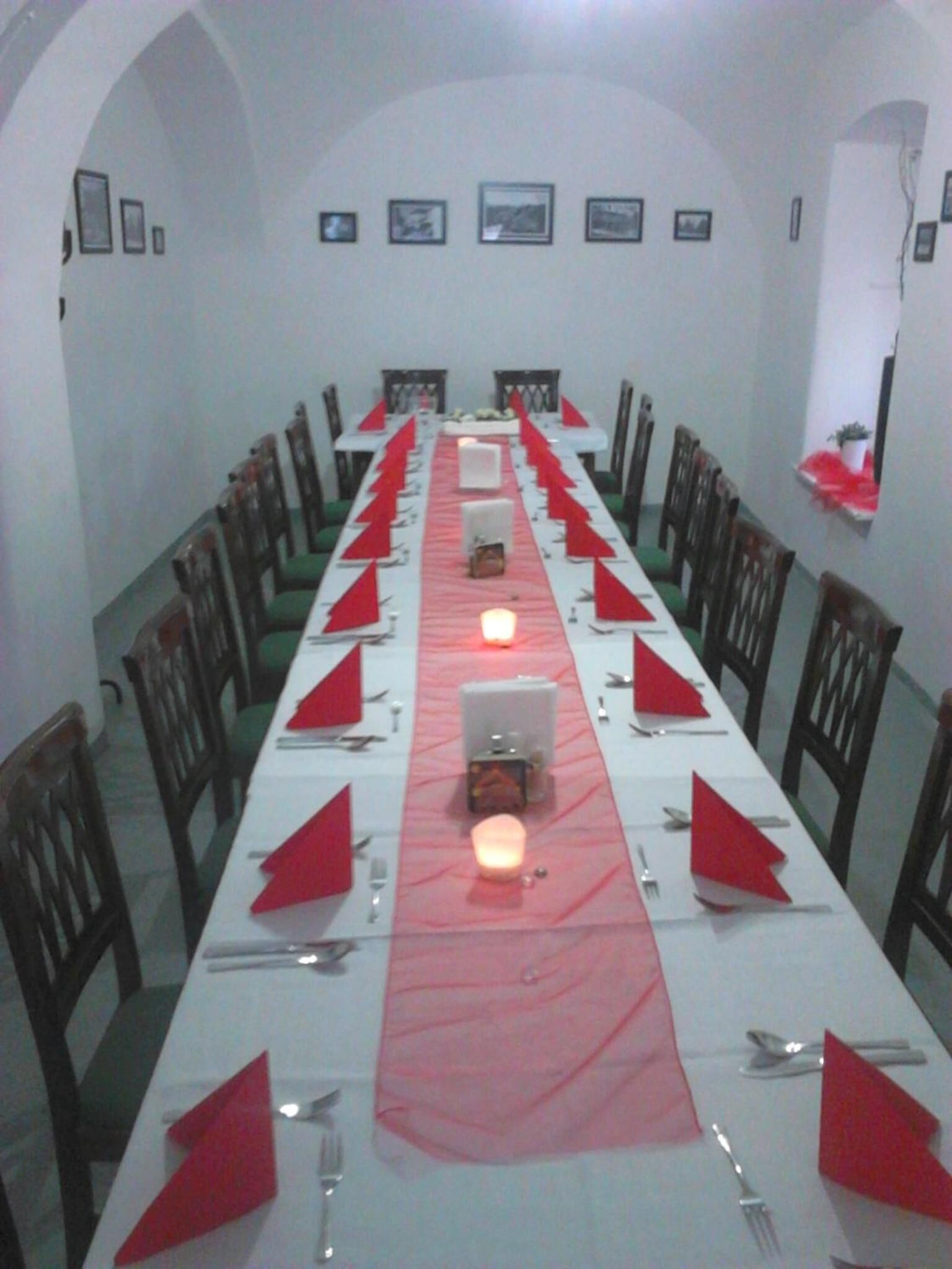 Una larga mesa de comedor dispuesta con servilletas rojas, cubiertos y velas, con sillas a cada lado.