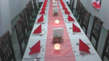 Una larga mesa de comedor dispuesta con servilletas rojas, cubiertos y velas, con sillas a cada lado.