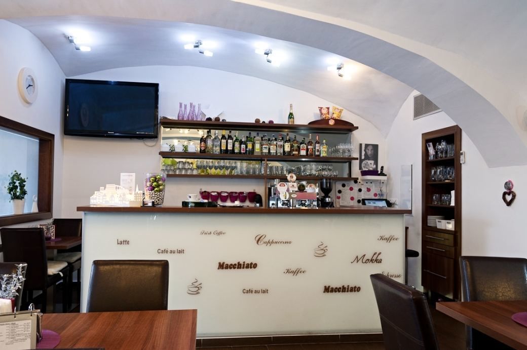 A bar area with shelves of bottles and glasses, a television mounted above the bar, and a wall with coffee-related text.