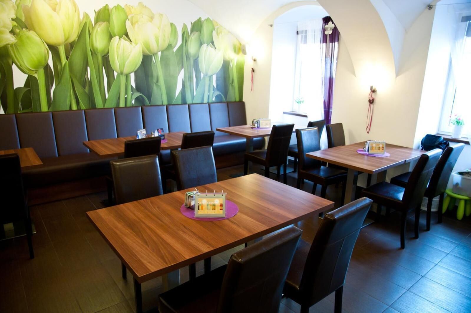 Een restaurant met zitplaatsen in hokjes en tafels, een groot muurschildering van tulpen en uitzicht op de straat door een rondboogvenster.