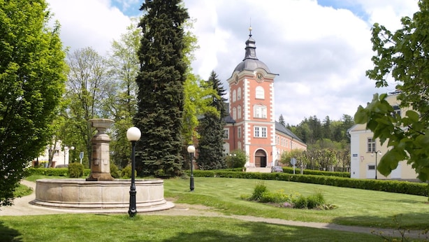 En park med en central fontän, ett högt klocktorn och en byggnad i bakgrunden.