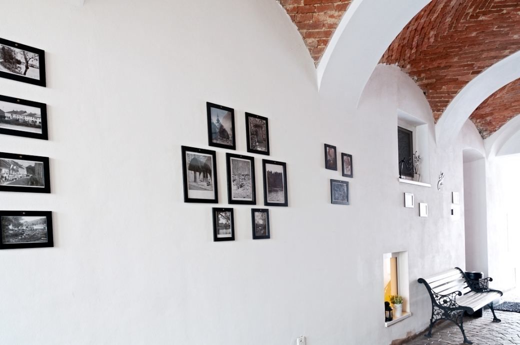 A corridor with white walls, black-framed photographs, and a brick ceiling.