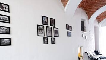 A corridor with white walls, black-framed photographs, and a brick ceiling.