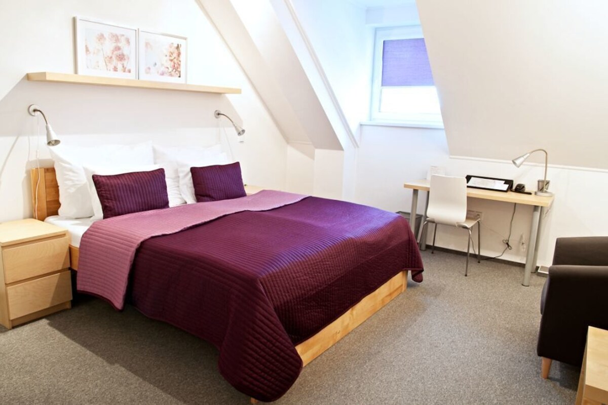 A bedroom with a bed, bedside tables, a desk, and a chair.