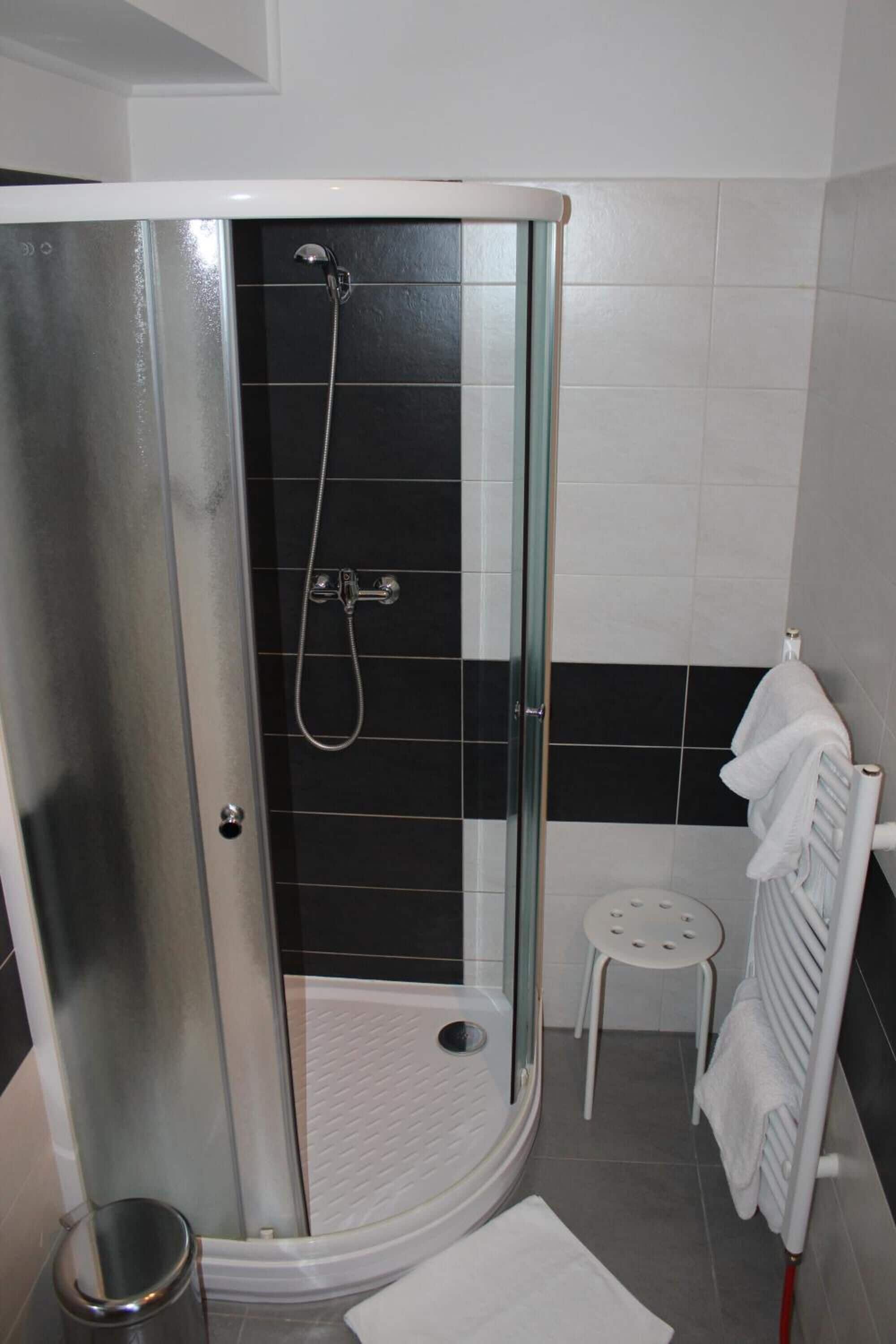 A modern bathroom with a glass-enclosed shower, a white toilet, and a small white stool.