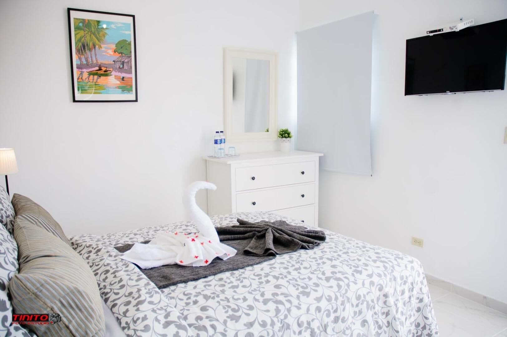 A hotel room with a bed, a dresser, a mirror, a TV, and a framed picture on the wall.