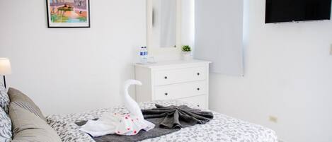 A hotel room with a bed, a dresser, a mirror, a TV, and a framed picture on the wall.