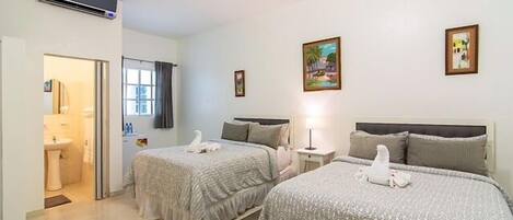 Habitación de hotel con dos camas, baño y una pequeña zona de estar.