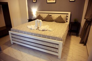 Una cama bien tendida con cabecera blanca y colcha estampada, junto con almohadones decorativos y una planta pequeña en una mesita de noche.