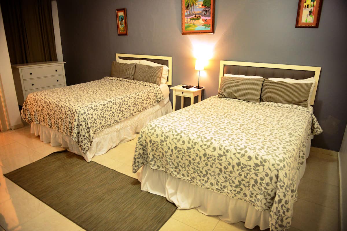 Dos camas matrimoniales con ropa de cama estampada con motivos florales, una mesita de noche con lámpara y un aparador pequeño.