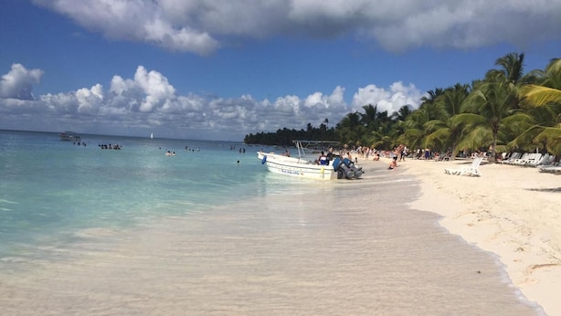 Een strand met helder turquoise water, een zandstrand en palmbomen.