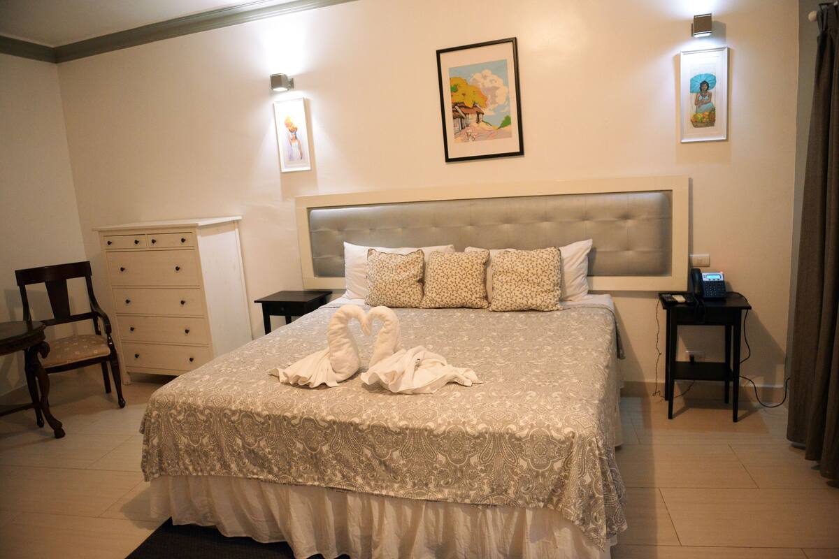 Un dormitorio con una cama grande, un tocador, una silla y obras de arte en las paredes.