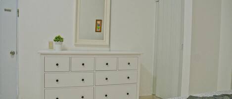 Un dormitorio con un aparador blanco, una cama con ropa de cama estampada, un cuadro en la pared y una puerta.