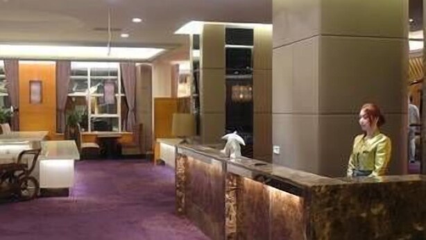 En hotellobby med en marmordisk i receptionen, ett lila golv och en sittgrupp med bord och stolar.