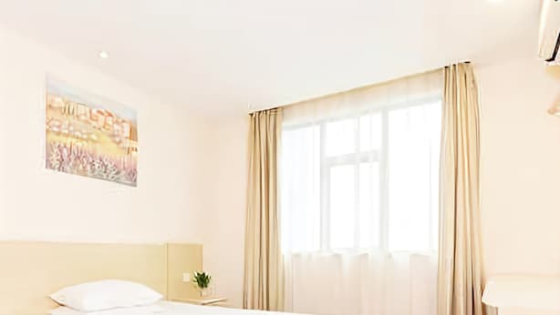 A hotel room with a large bed, a bedside table with a lamp, a window with curtains, and a painting on the wall. - Hanting Hotel (Shaoxing)