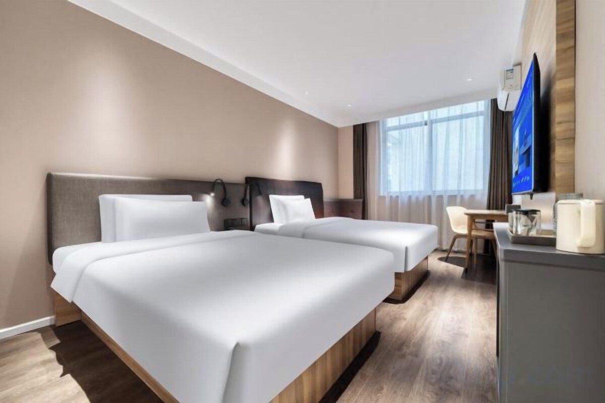 A hotel room with two beds, a desk, a chair, and a television.