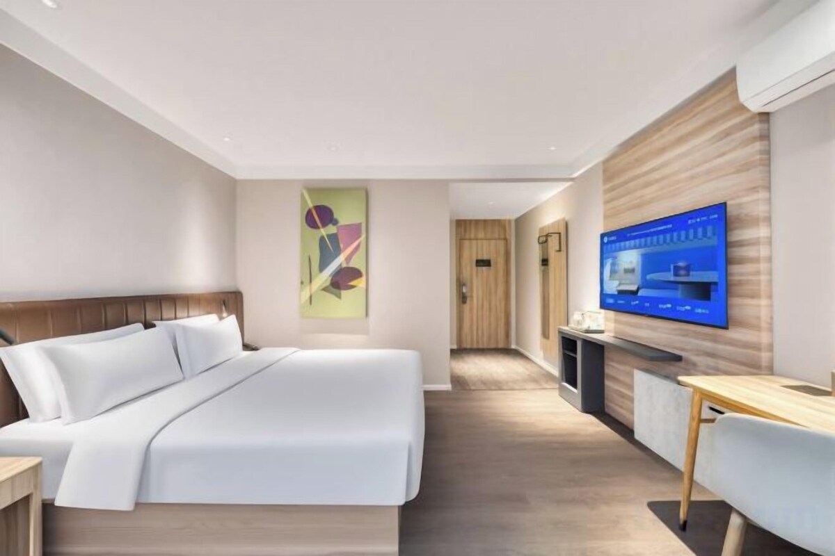 A modern hotel room with a large bed, a desk, a television, and a bathroom visible through an open door.