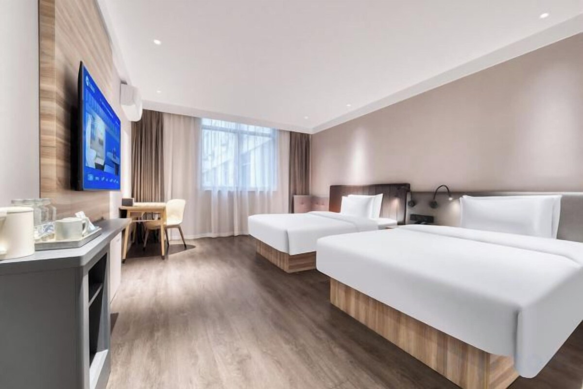 A hotel room with two beds, a desk, a TV, and a window with curtains.