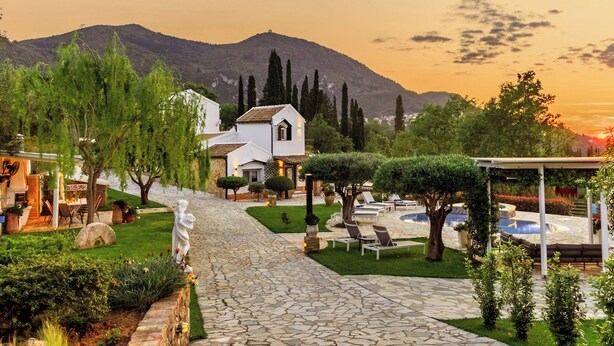 A stone pathway leading to a white building with a garden and outdoor seating area. - Villa Claire Corfu (Corfu)