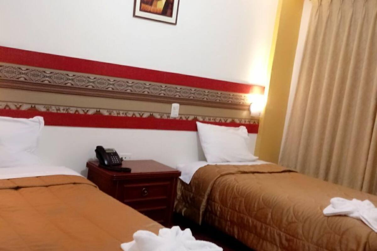 A hotel room with two beds, a telephone on a nightstand, a framed picture on the wall, and a window with curtains.