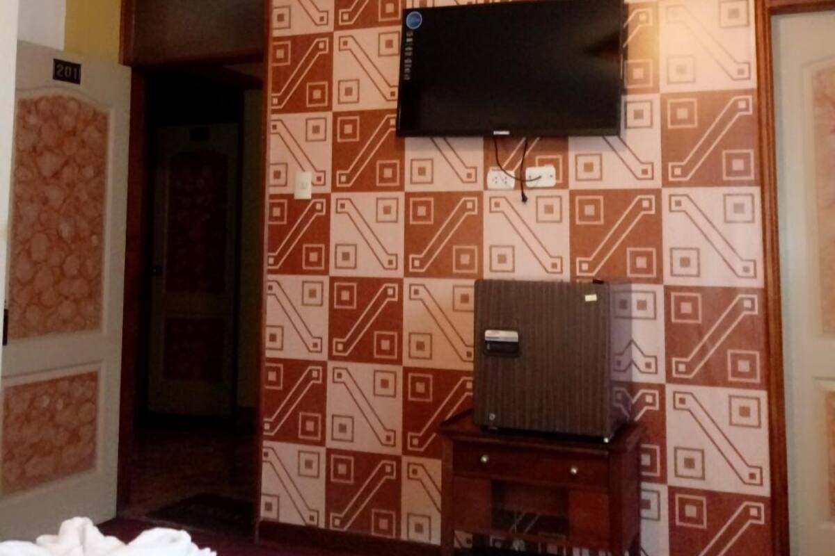 A hotel room with a bed, a television mounted on the wall, and a patterned wallpaper.