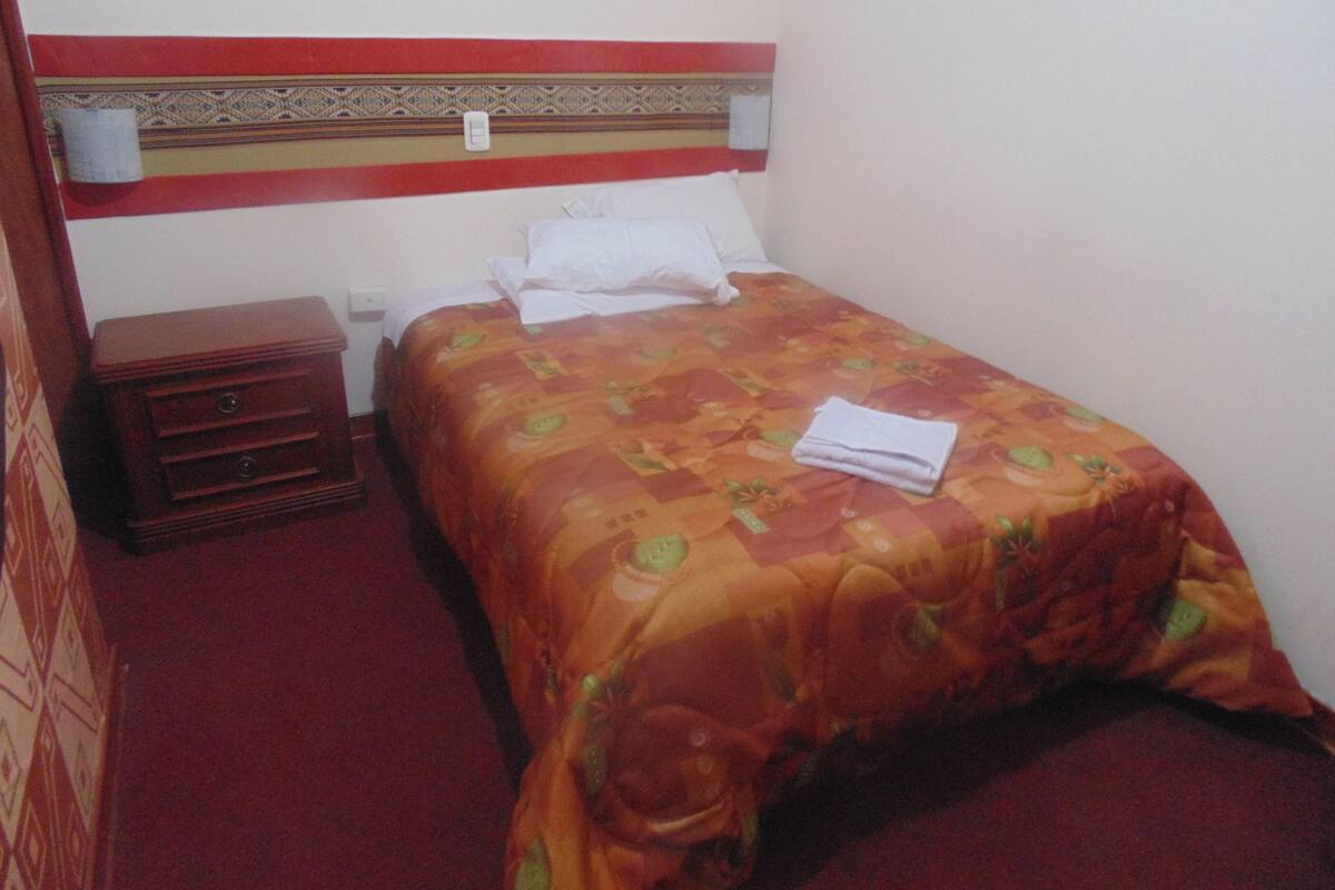 A hotel room with a bed, a nightstand, and a wall-mounted light.