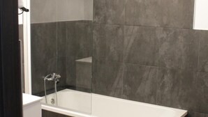 A modern bathroom with a glass-enclosed shower, dark tiled walls, and a wooden floor. - Suites A Coruña (A Coruña)