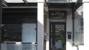 A building entrance with a glass door, a sign for 'Suites Coruna', and a website address. - Suites A Coruña (A Coruña)