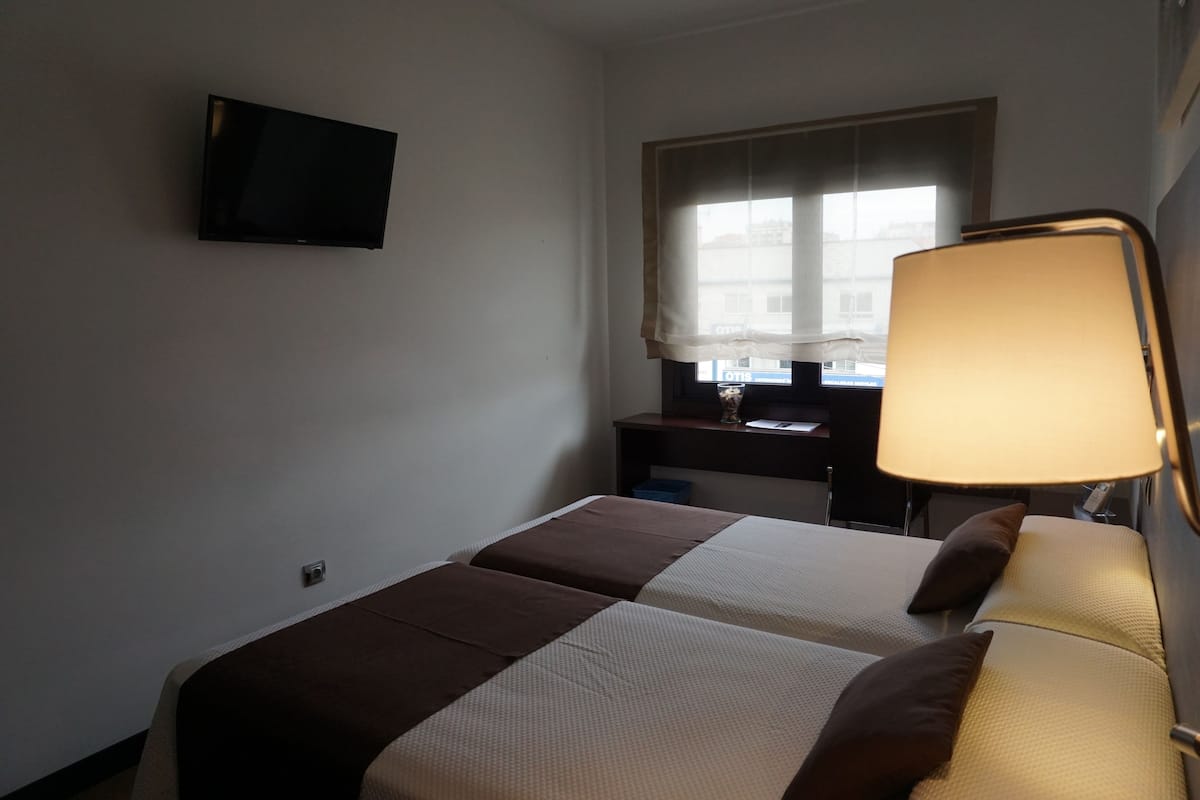 A hotel room with a bed, a desk, a lamp, and a TV on the wall.