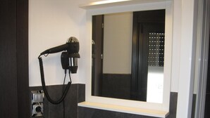 A bathroom with a hairdryer mounted on the wall, a mirror, and a tiled floor. - Suites A Coruña (A Coruña)