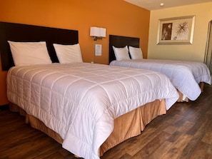 A hotel room with two beds, wooden flooring, and a framed picture on the wall. - Stamford Inn (Stamford)