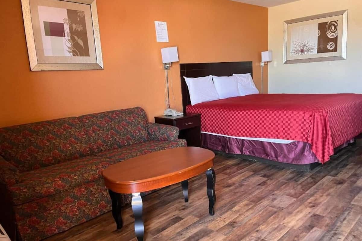 A hotel room with a bed, a sofa, a table, and two framed pictures on the walls.