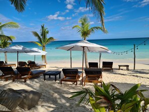 A beach with lounge chairs and umbrellas, palm trees, and a clear view of the ocean. - Gramercy Tulum (Tulum)