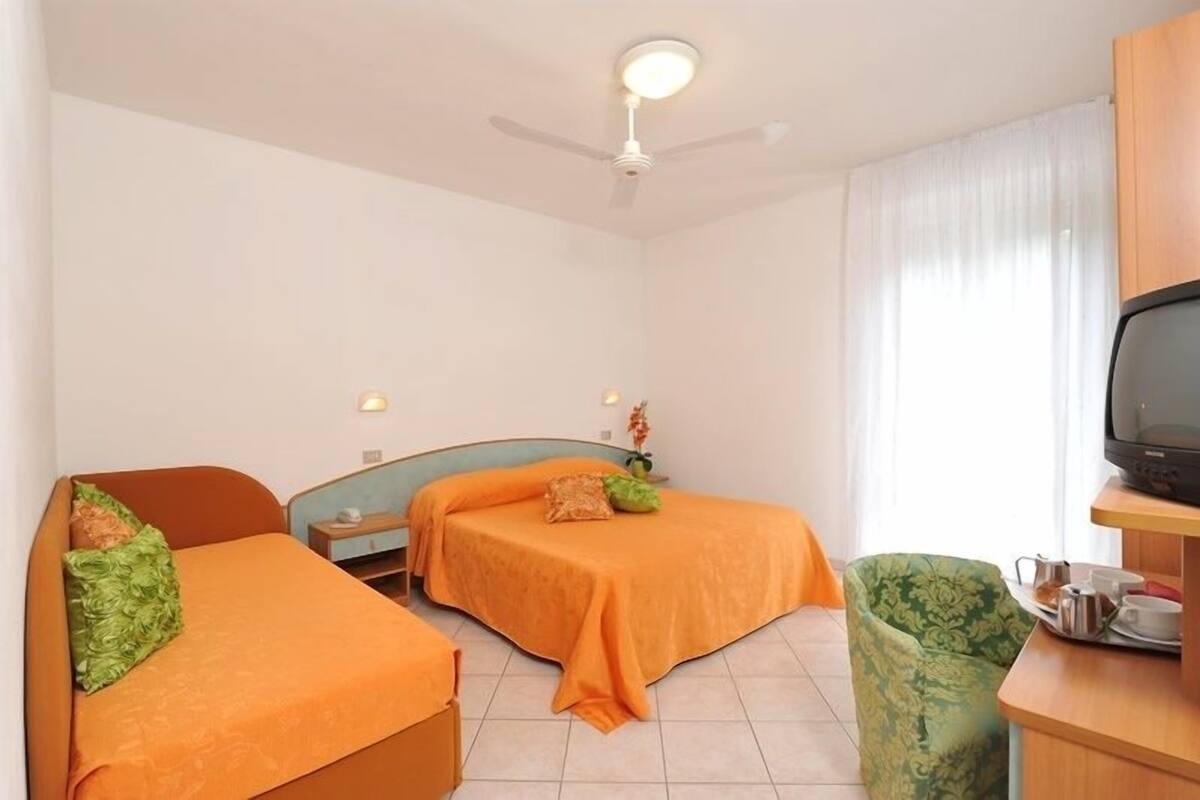 A hotel room with two beds, a television, a desk with a chair, and a ceiling fan.