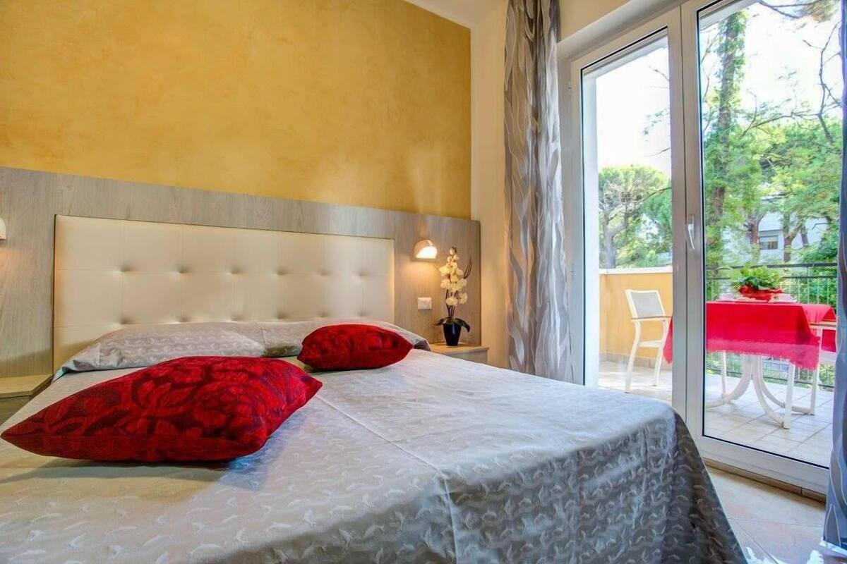 A bedroom with a large bed, a headboard, a nightstand, and a window with a view of the outdoors.